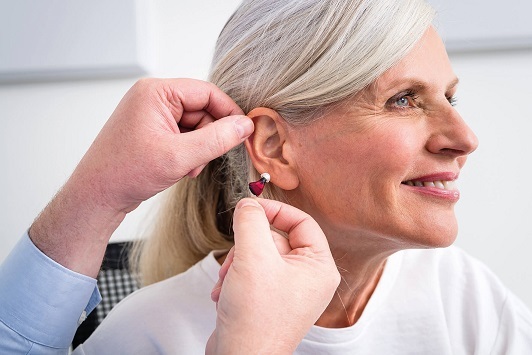 Ältere Frau erhält Hörgerät von Hörakustiker, Hörgeräteanpassung und Hörhilfe-Beratung.